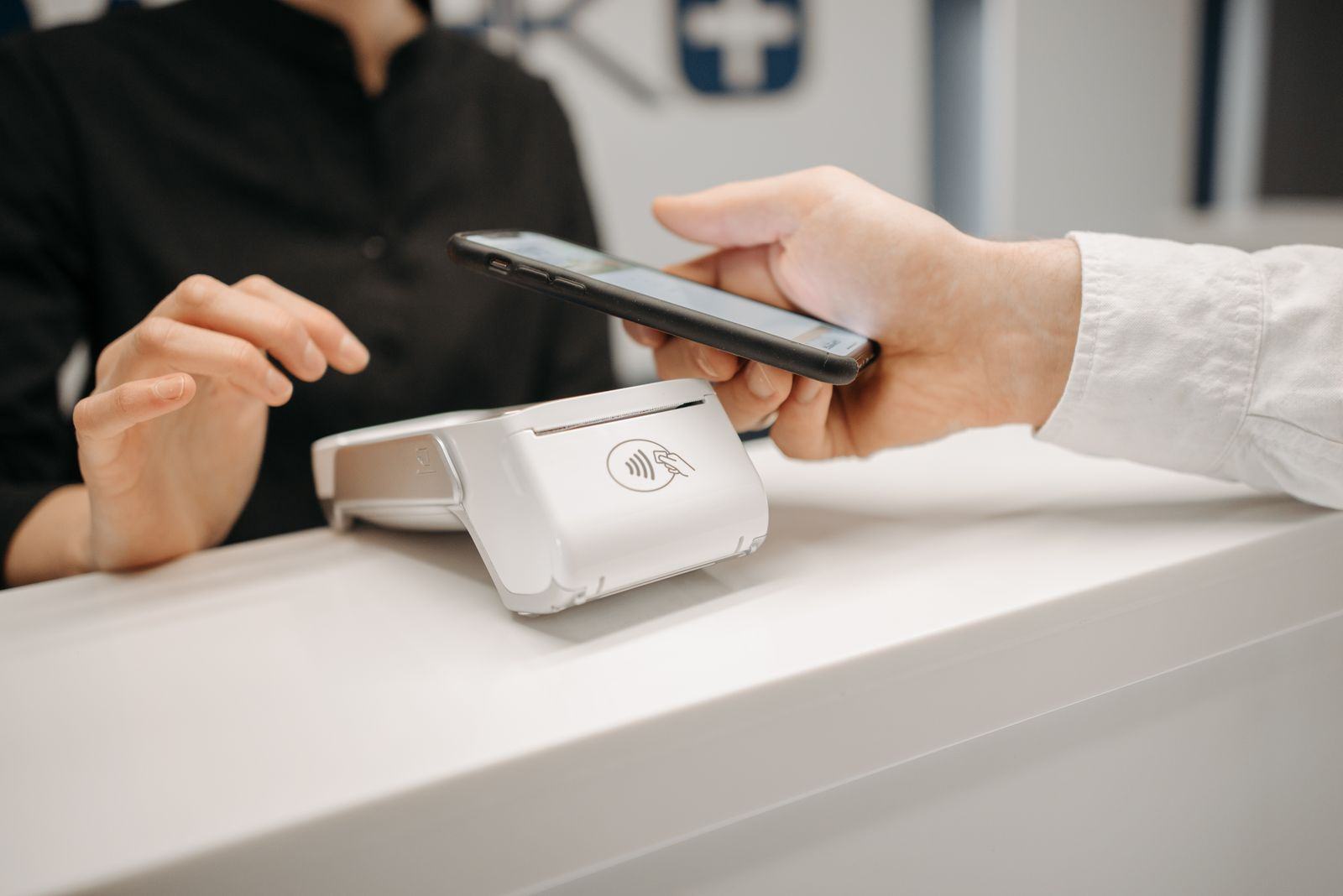 A customer holding a phone near a contactless reader at a shop counter